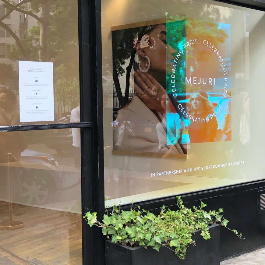 Storefront with blue/orange-appearing holographic film with Mejuri Pride logo.